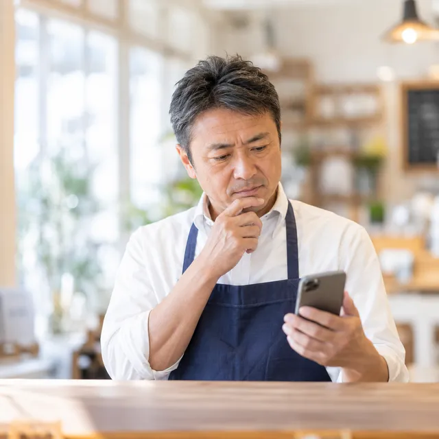 スマートフォンの画面を見ながら考え込んでいる、店の主人